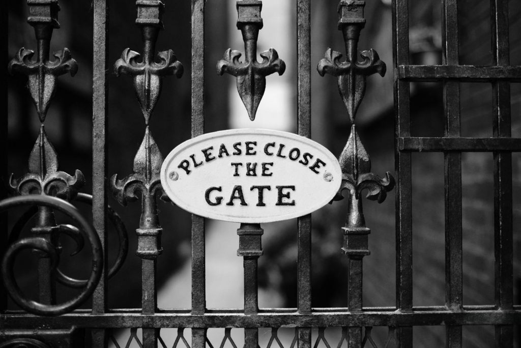 Close-up of a vintage iron gate with a 'Please Close the Gate' sign in black and white.